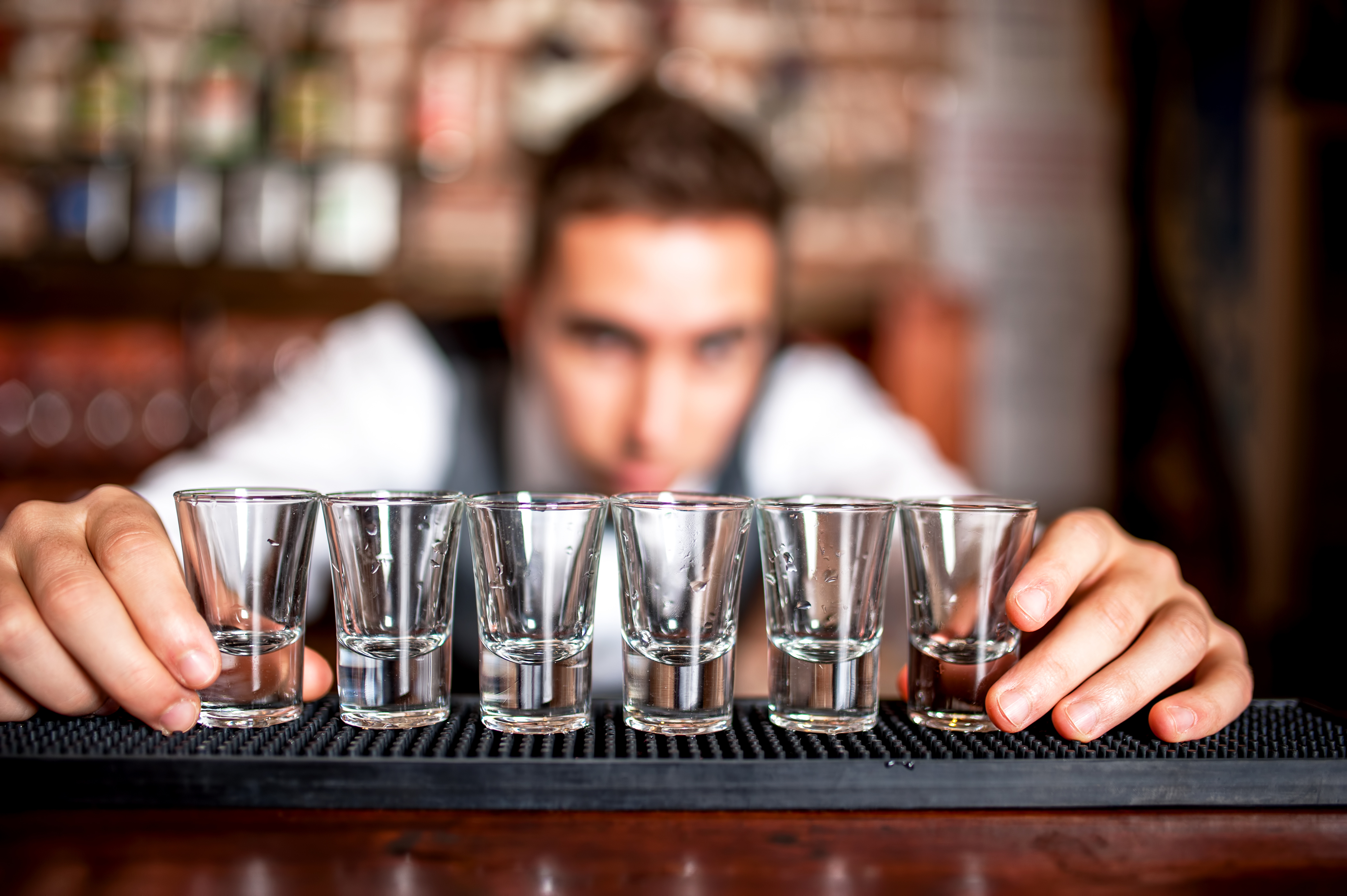 bartender preparing and lining shot glasses for alcoholic drinks on bar